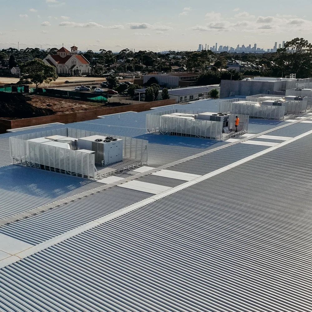 Large rooftop with multiple HVAC units, surrounded by urban landscape and distant city skyline.