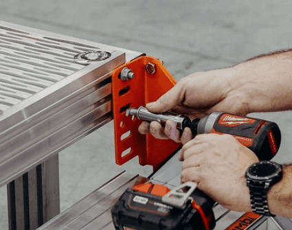 Person using a power drill to secure a metal bracket on an industrial workbench with precise alignment.