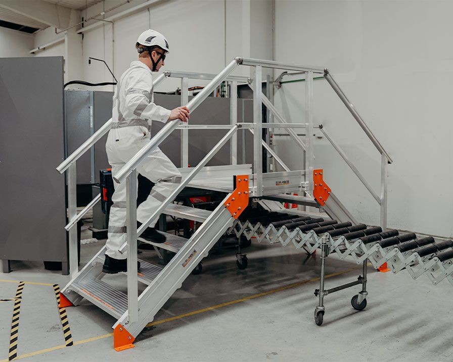 Person in protective gear walking up metal stairs beside a conveyor belt in an industrial setting.