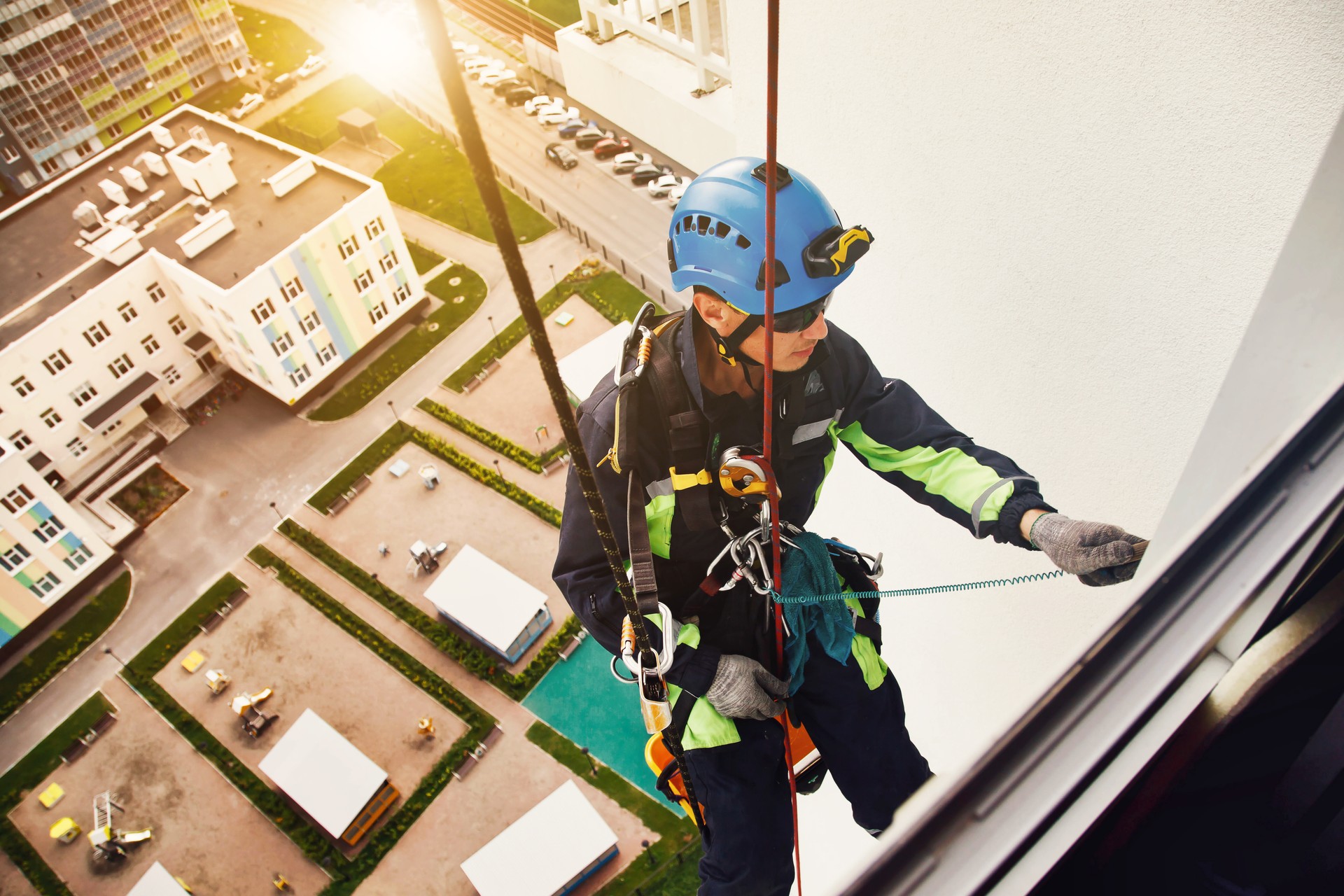 Industry urban works. Rope access laborer on wall of house. Top view of industrial mountaineering worker in uniform hangs over residential building at background, washing exterior facade. Copy space